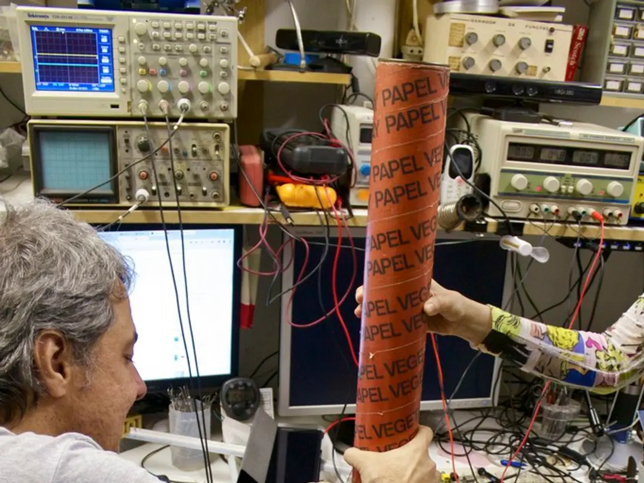 In this image we can see machines, cables, computer display, pen holder, persons and a stress ball.