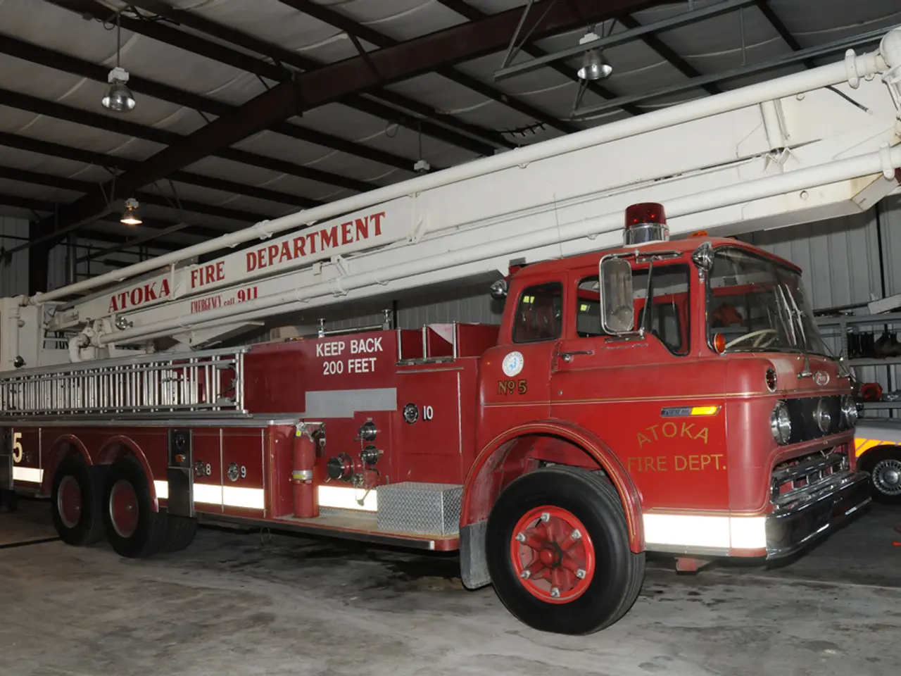 In the image there is a fire engine inside a godown and there are lights over the ceiling.