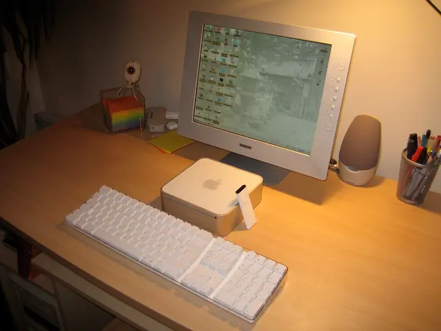 In this image on a table there is a monitor, keyboard, remote, speaker, a pen stand with pens, and...