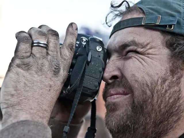 In this image we can see there is a person holding a camera and taking pictures. And he kept a cap...